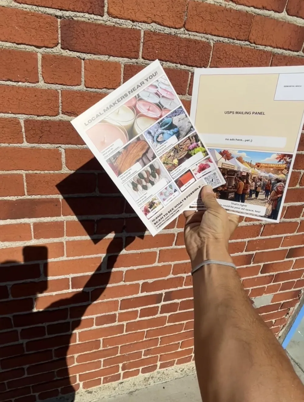 Jeremy holding the printed front and back of the Paradox Postcards card against a brick wall